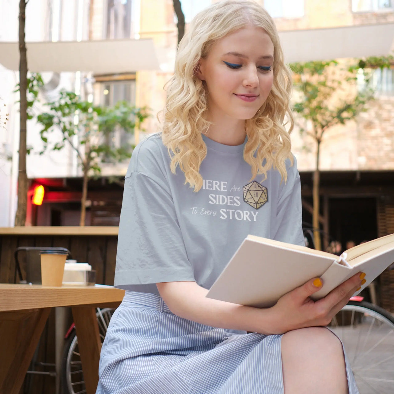 woman reading wearing a light blue There are 20 sides to every story tshirt with white text