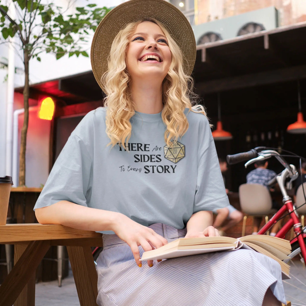 woman in a hat laughing while wearing an oversized light blue There are 20 sides to every story tshirt