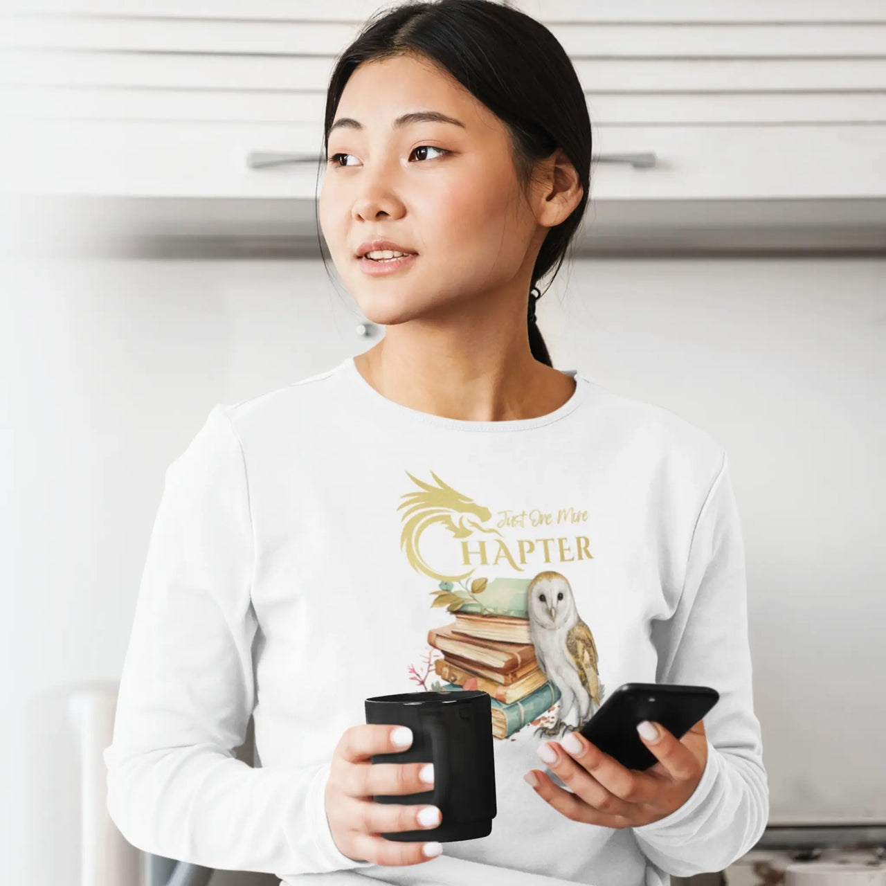 woman having a coffee wearing her Just One More Chapter long sleeve shirt V2 in white with gold design