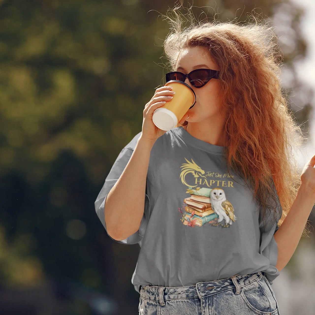 woman drinking coffee wearing the Dark grey Just One More Chapter Tshirt V2 with gold text