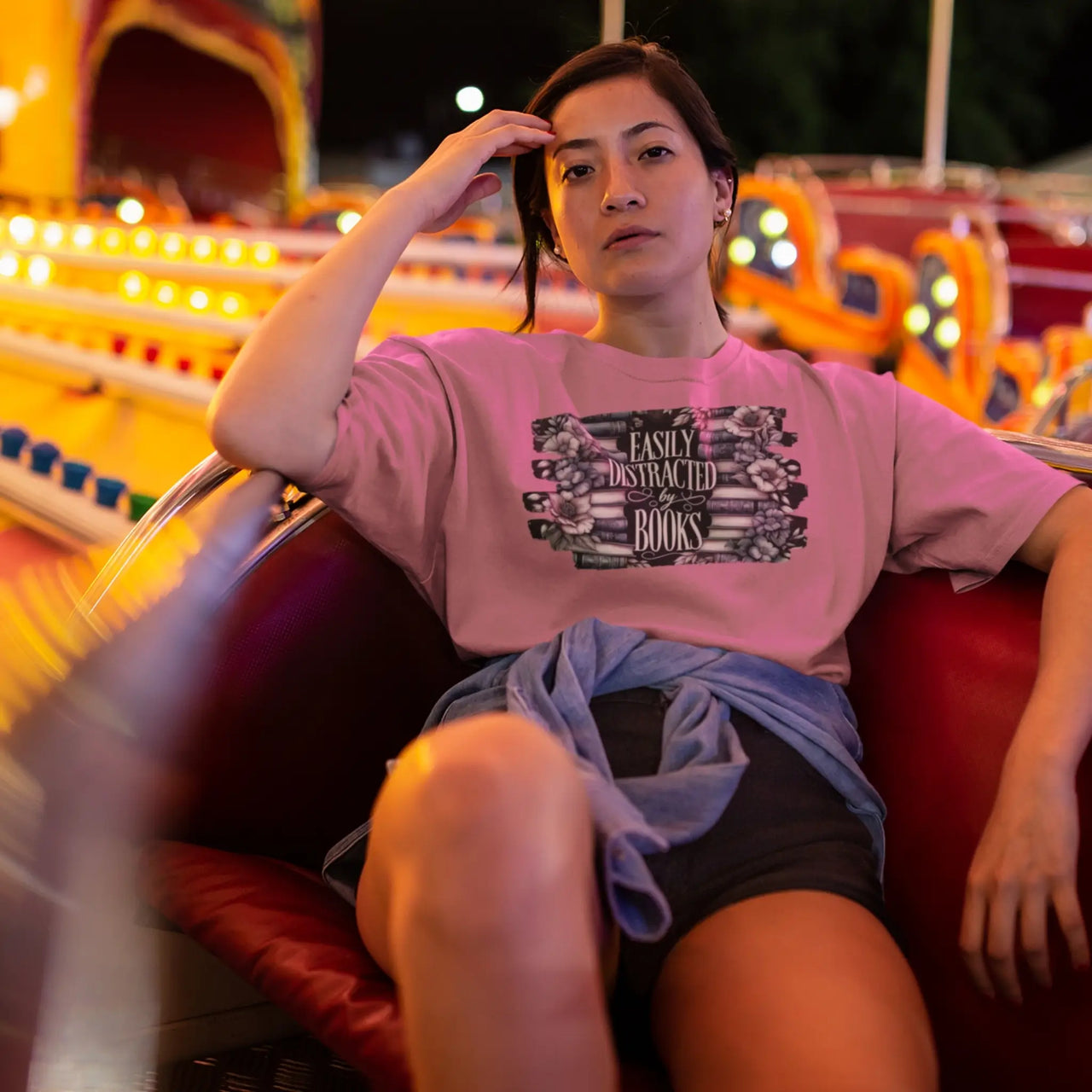 woman in a seat wearing a dark pink Easily distracted by books tshirt