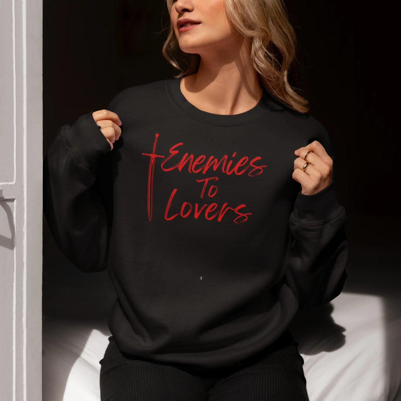 woman showingoff her black Enemies To Lovers sweatshirt with red text