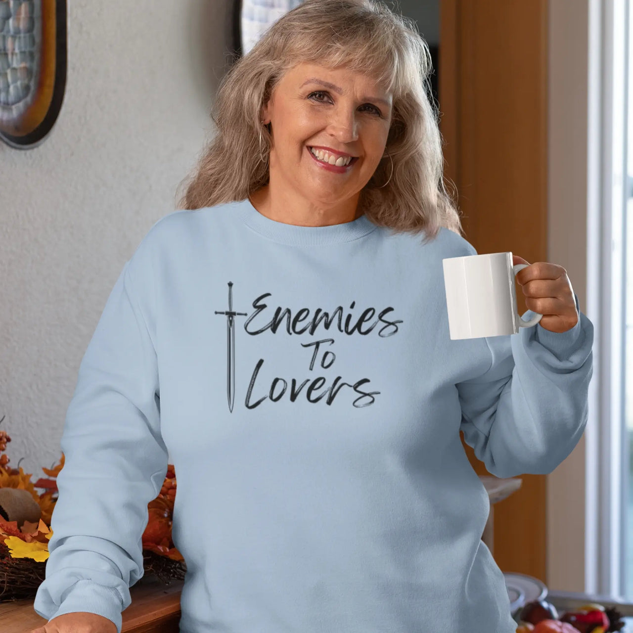 woman drinking coffee wearing a blue Enemies To Lovers sweatshirt