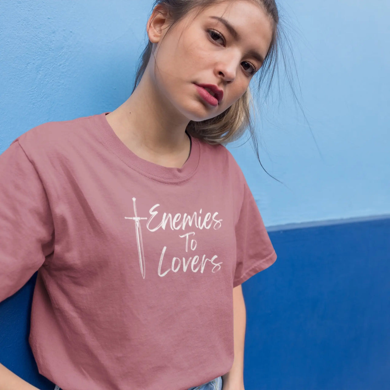 woman leaning against a wall wearing  dark pink Enemies To Lovers Tshirt with white writing