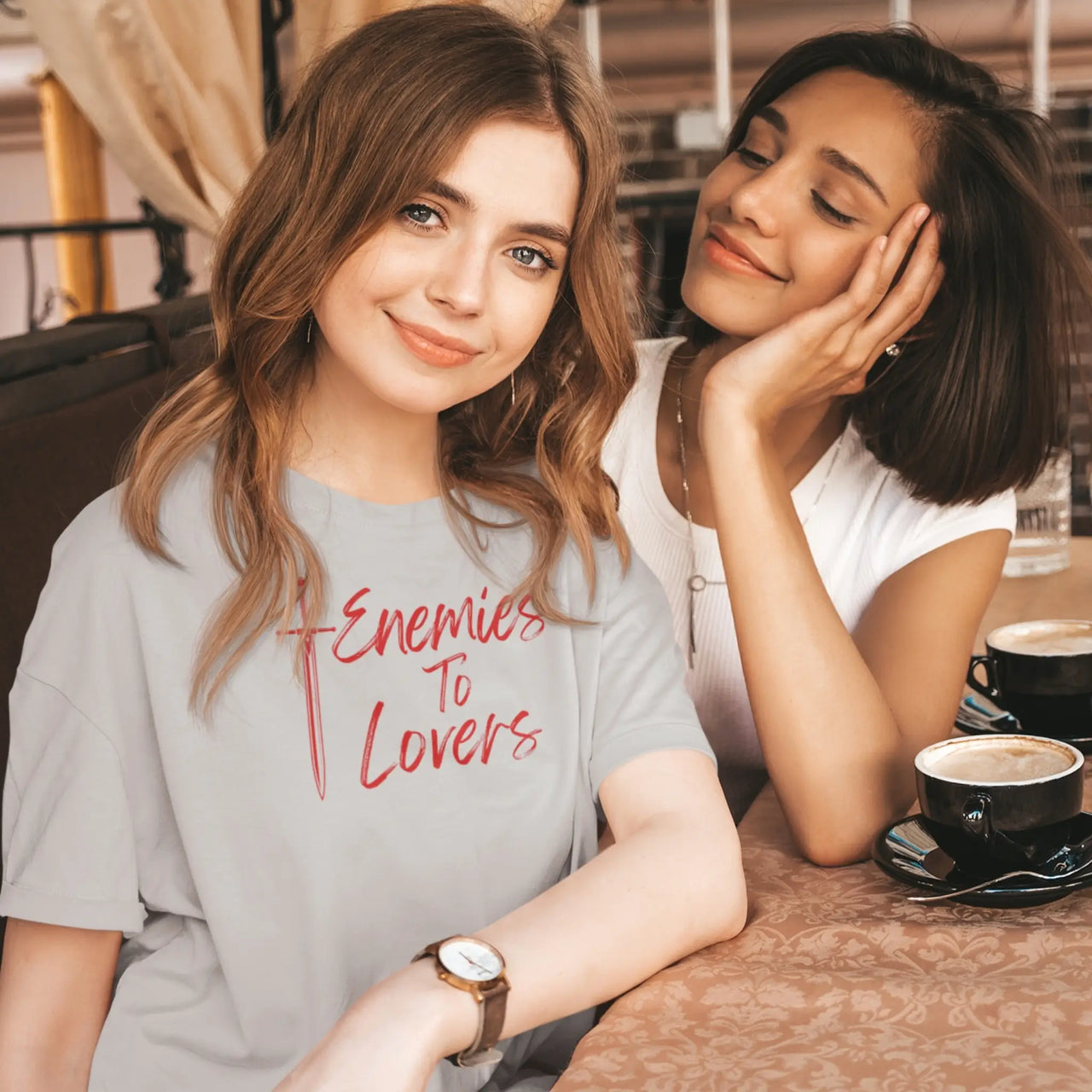 young woman wearing a light grey enemies to lovers tee with red text