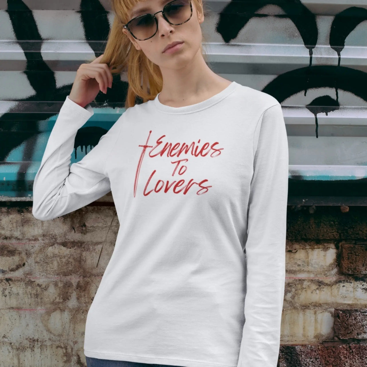 woman with sunglasses wearing a Enemies To Lovers Long Tshirt in white with red text