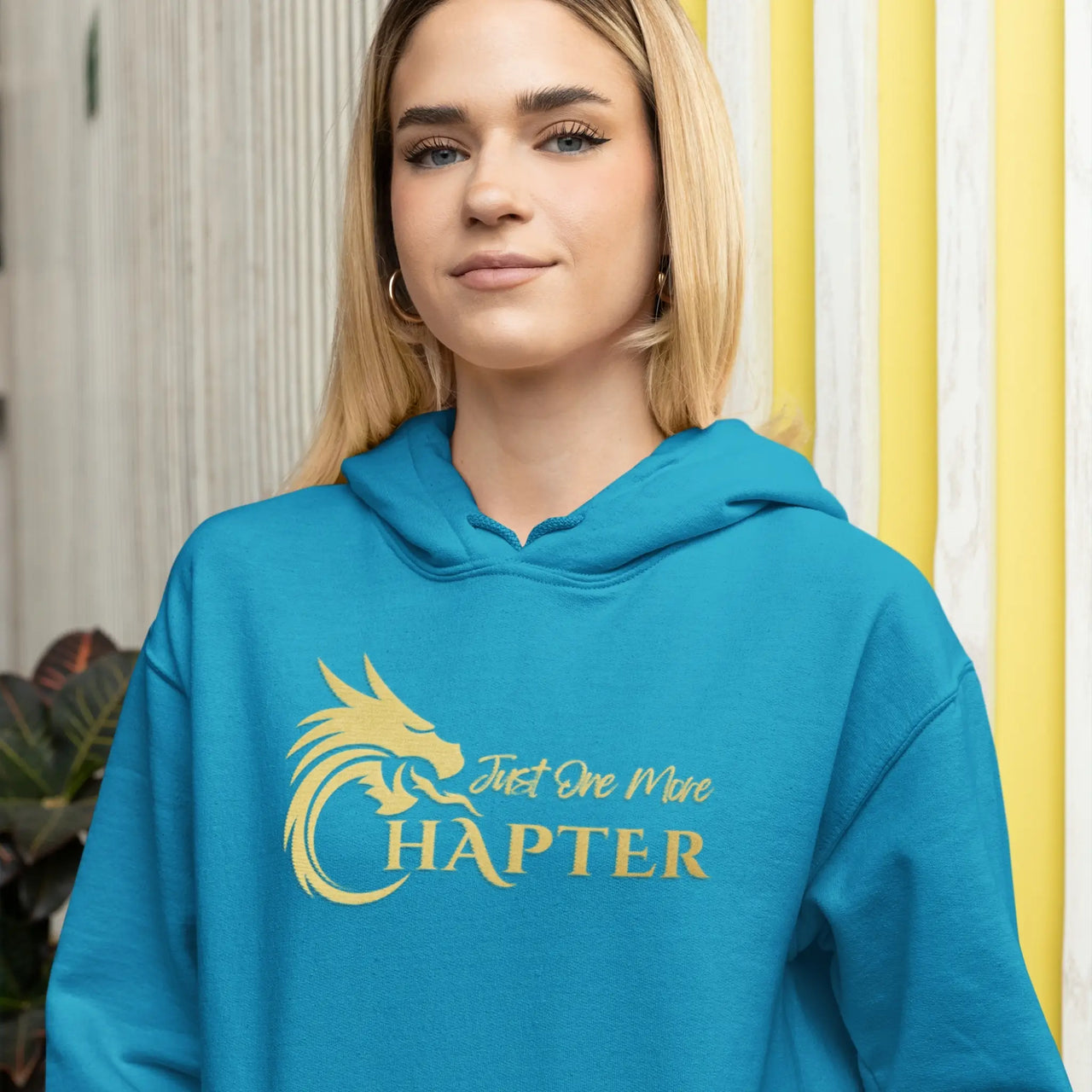 a woman wearing a teal Just One More Chapter Hoodie V1 with gold text