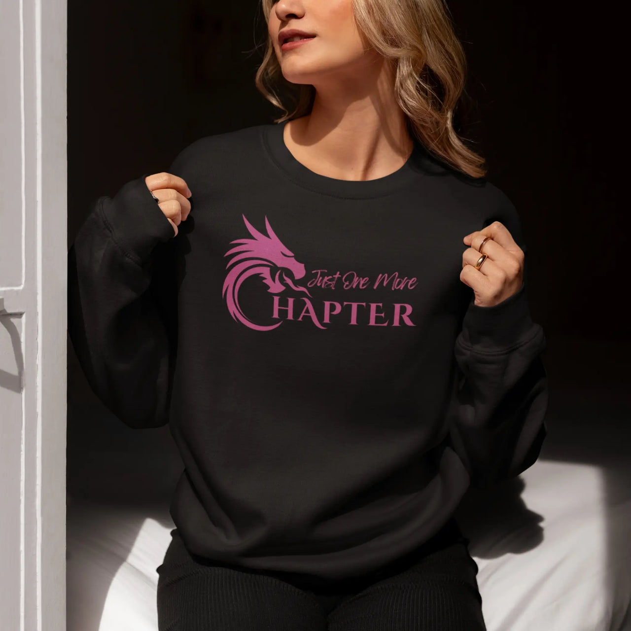 woman wearing a black Just One More Chapter sweatshirt with purple text