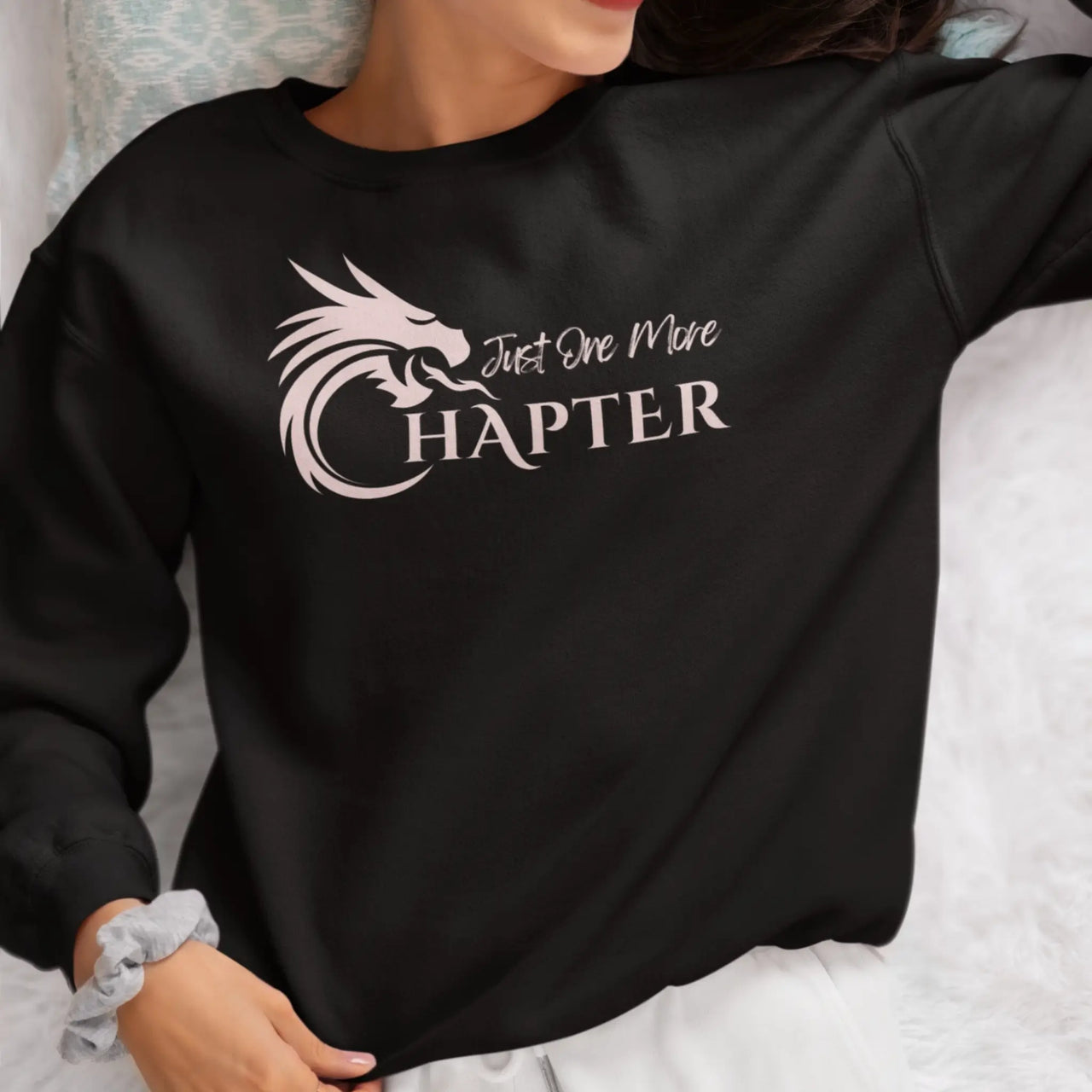 Woman wearing a black Just One More Chapter sweatshirt with pink text