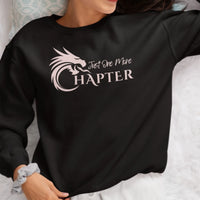 Thumbnail for Woman wearing a black Just One More Chapter sweatshirt with pink text