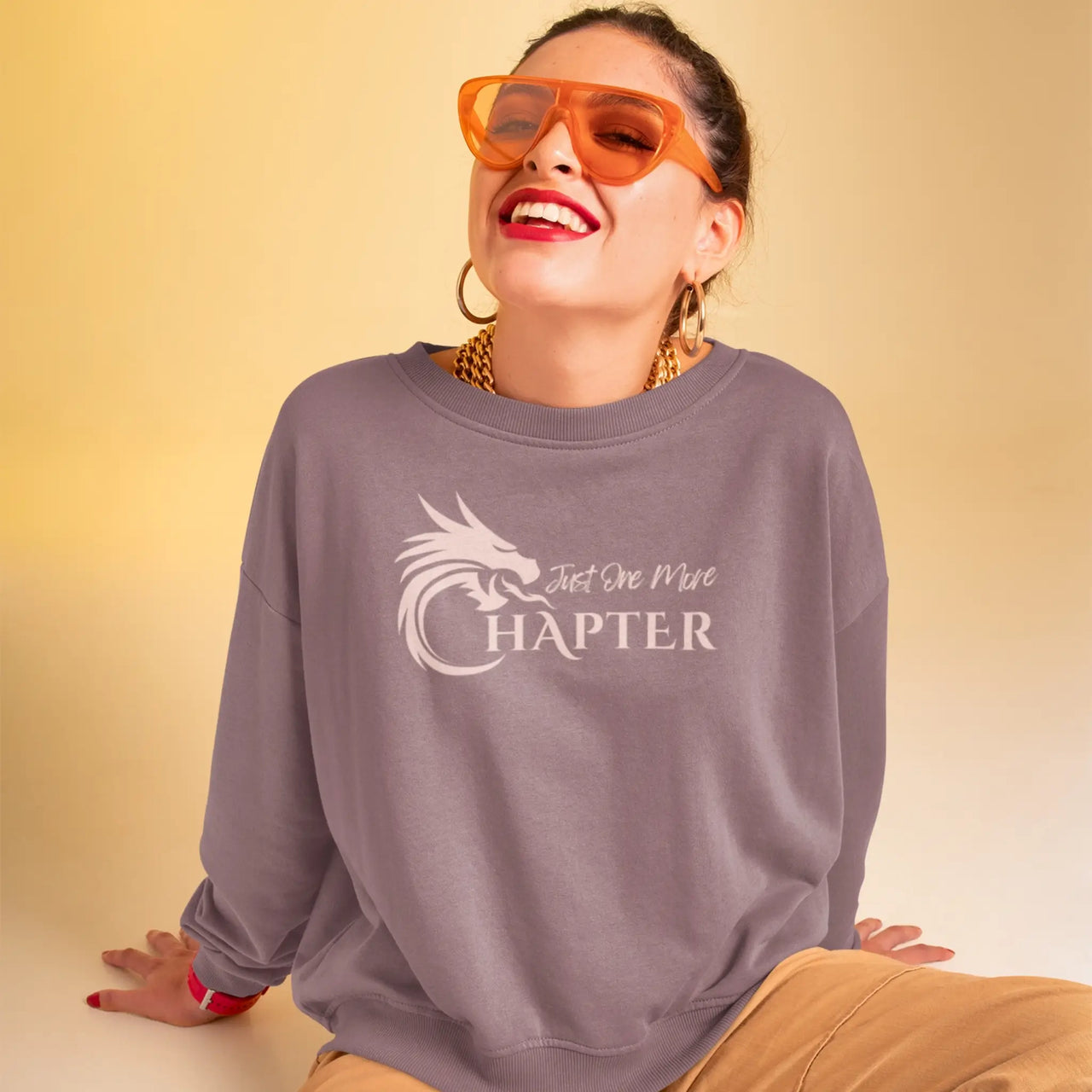 woman with sunglasses wearing a maroon Just One More Chapter sweatshirt with pink text