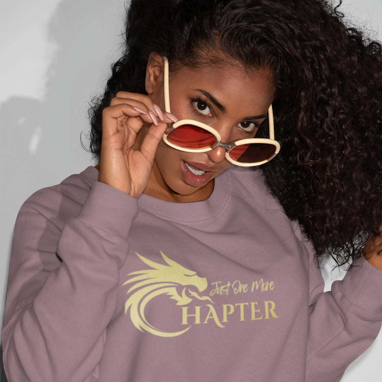 woman wearing a maroon Just One More Chapter sweatshirt with gold text