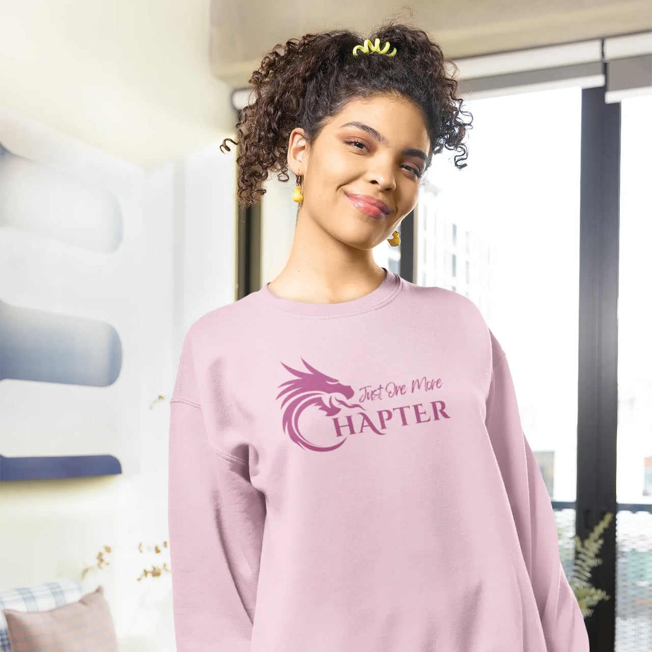 smiling woman wearing a Pink Just One More Chapter sweatshirt with purple text