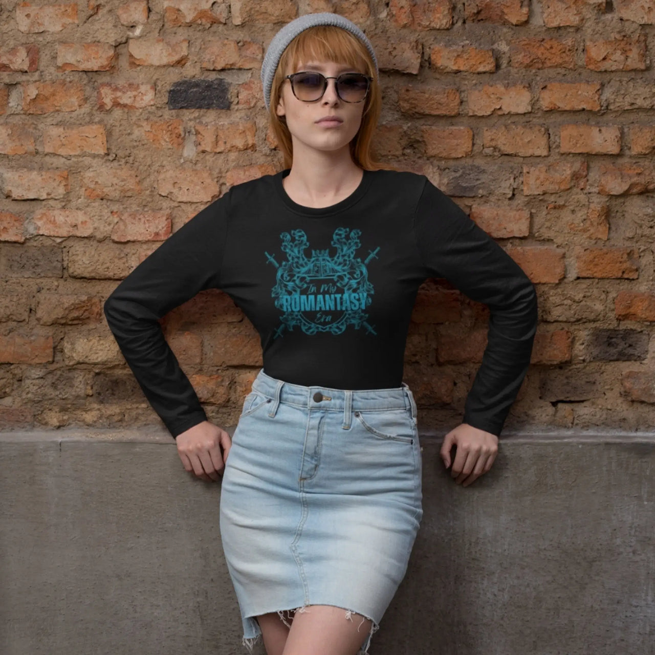 woman in front of a wall showing off an In My Romantasy Era shirt on black with teal text