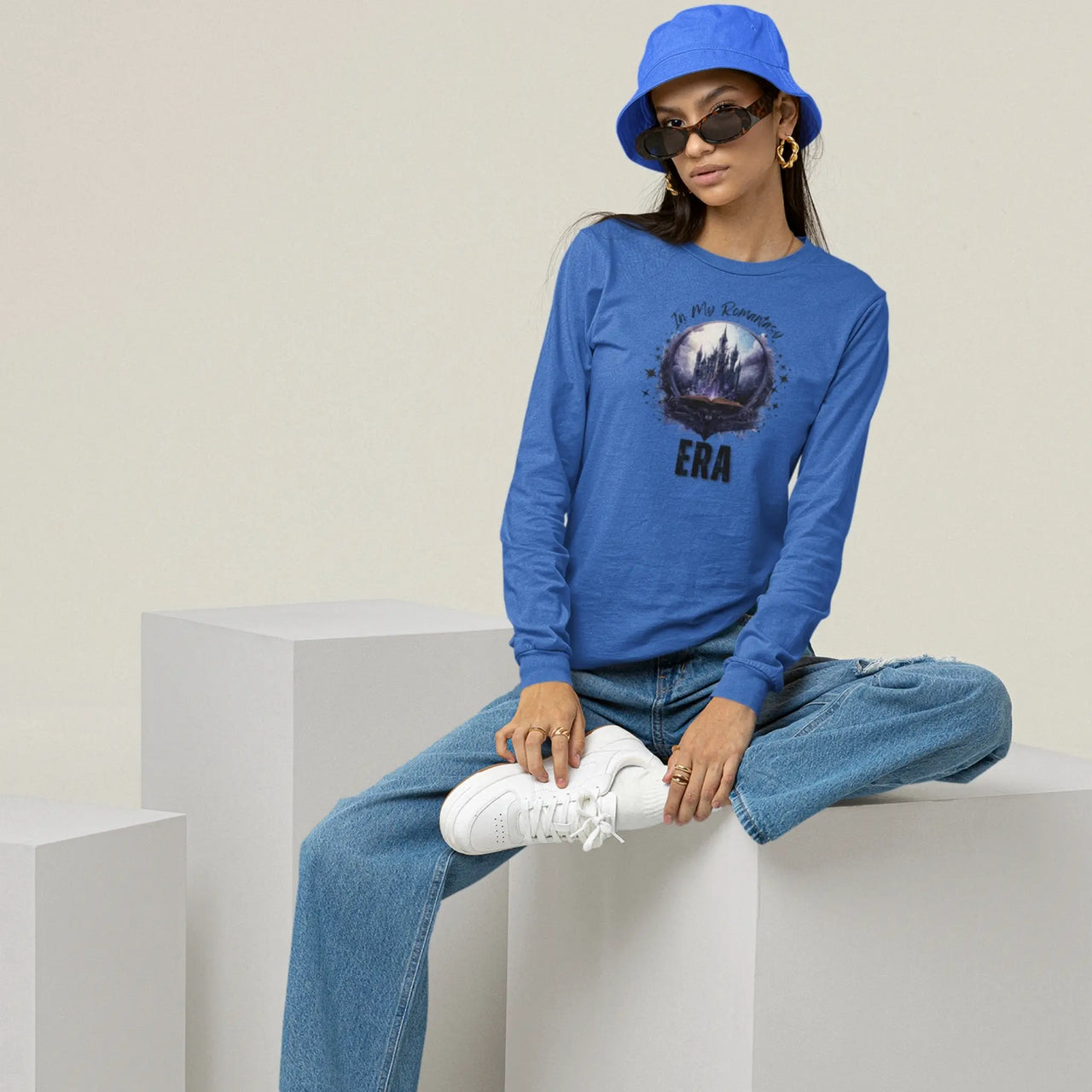 young woman with a hat and glasses wearing an In My Romantasy Era V2  long sleeve on blue