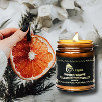 Thumbnail for lit Winter Grove Candle with citrus and evergreens around it